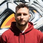 Uomo con felpa rossa davanti a un murales.
